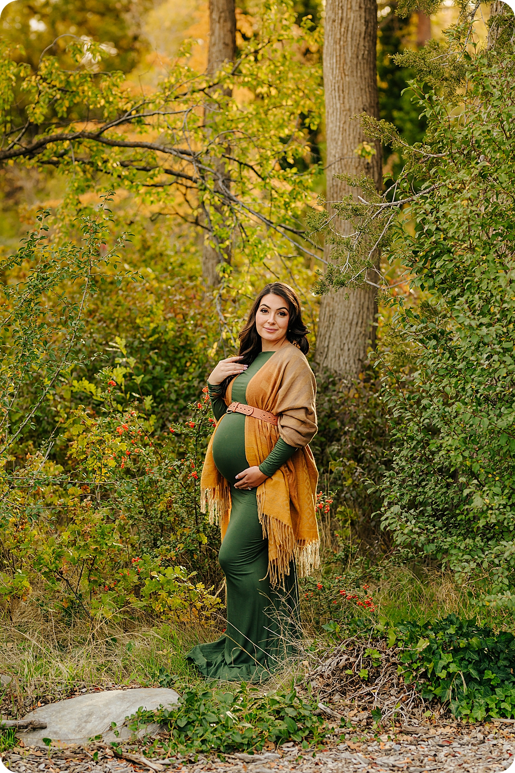 mom stands in woods with baby belly in green dress