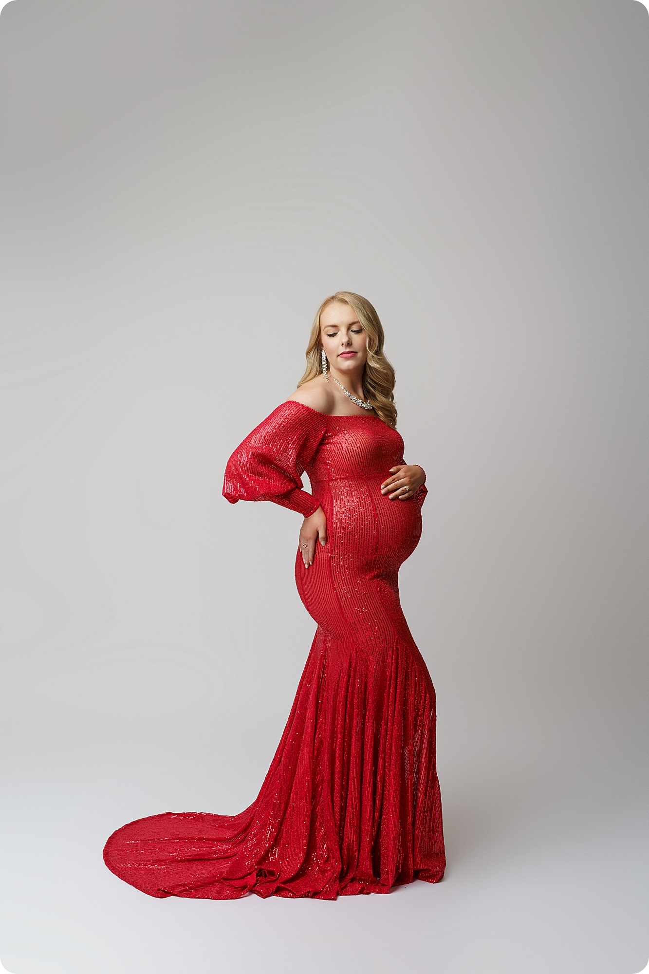 woman in red dress holds stomach during dramatic studio maternity portraits