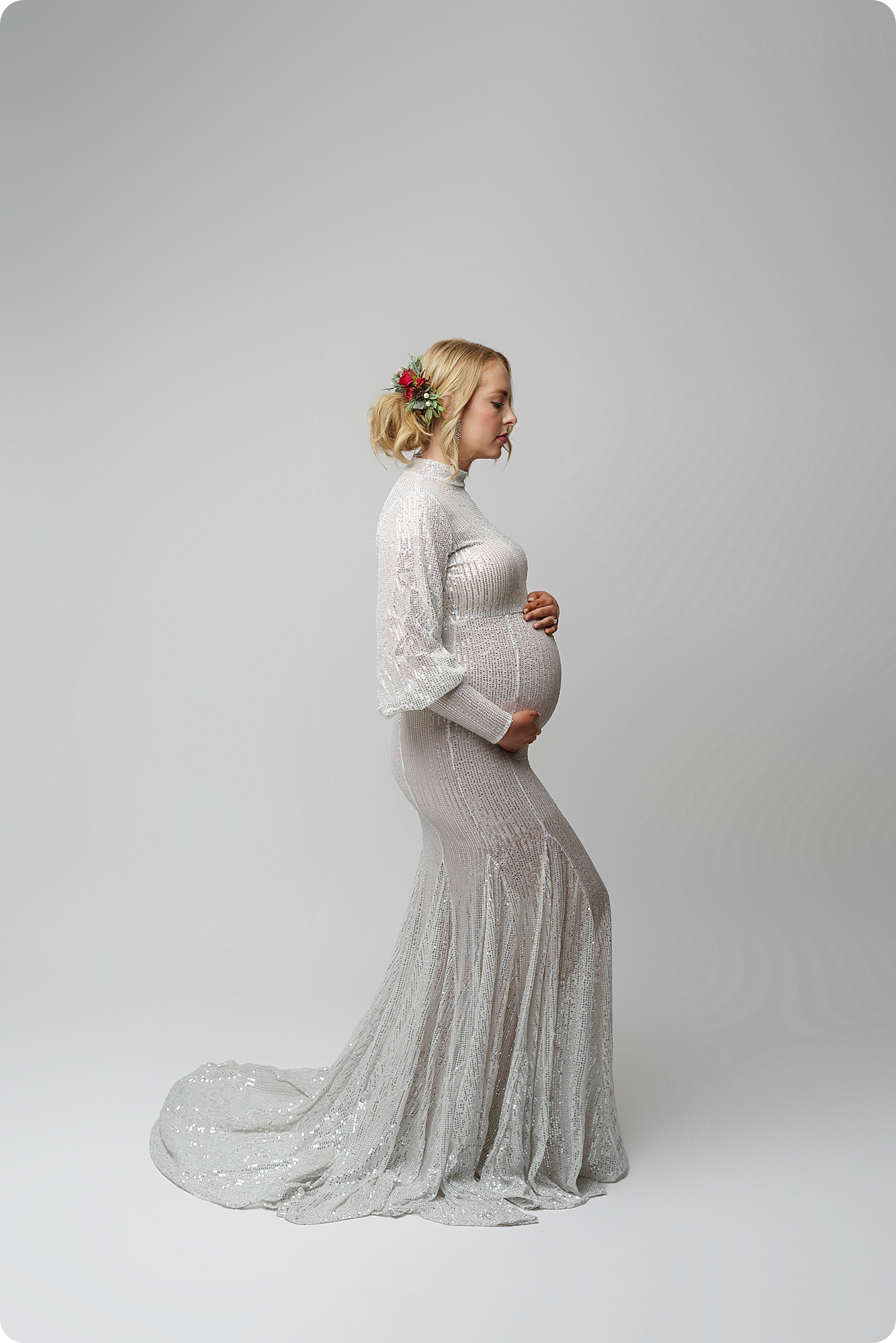 mom in white gown holds belly during studio maternity portraits
